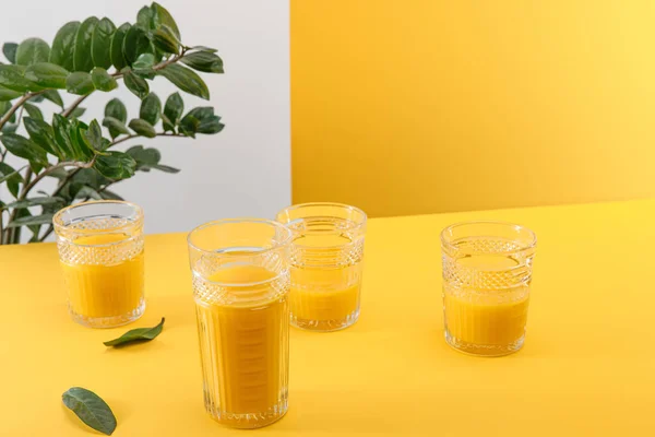 Gläser frischer köstlicher gelber Smoothie in der Nähe grüner Pflanzen — Stockfoto