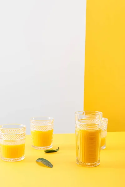 Copos de smoothie amarelo delicioso fresco perto de folhas verdes — Fotografia de Stock