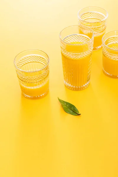 Glasses of fresh delicious yellow smoothie near green leaf — Stock Photo