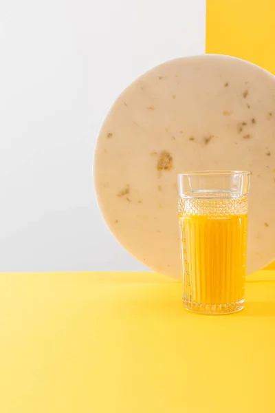 Glass of fresh delicious yellow smoothie near marble circle on grey and yellow background — Stock Photo