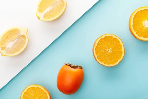 Vista superior de las mitades de naranja y limón con caqui sobre fondo azul y blanco - foto de stock