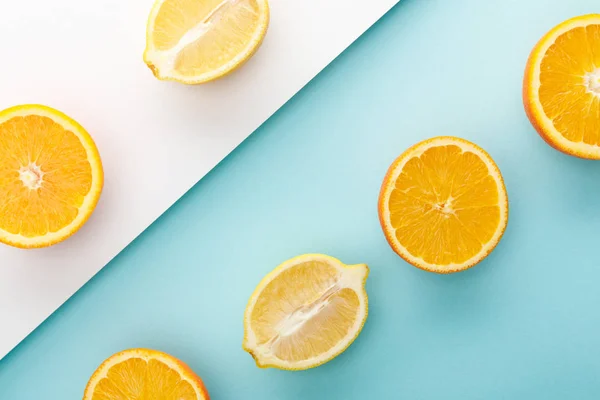 Vue de dessus des oranges coupées et des moitiés de citron sur fond bleu et blanc — Photo de stock