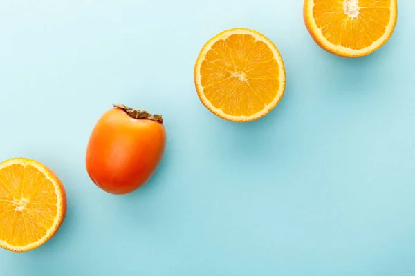 Draufsicht auf Orangenhälften und Kaki auf blauem Hintergrund — Stockfoto