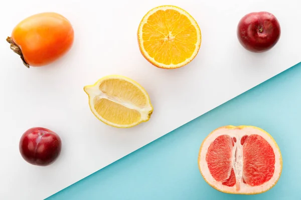 Vista superior de las mitades de naranja, limón y pomelo con caqui, manzanas sobre fondo blanco y azul — Stock Photo