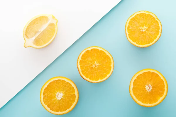 Draufsicht auf geschnittene Orangen und Zitronenhälfte auf weißem und blauem Hintergrund — Stockfoto