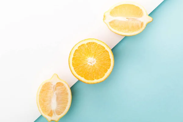 Vue de dessus des demi-oranges et des moitiés de citron sur fond blanc et bleu — Photo de stock