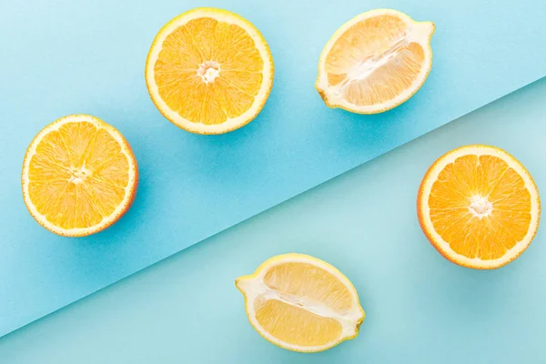 Vue de dessus des oranges coupées et des moitiés de citron sur fond bleu — Photo de stock