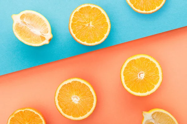 Vista superior de naranjas cortadas y mitades de limón sobre fondo azul y naranja - foto de stock