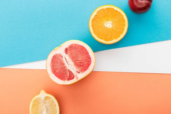 Draufsicht auf Obsthälften und Apfel auf blauem, orangefarbenem und weißem Hintergrund — Stockfoto