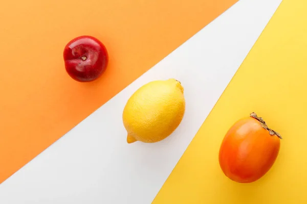 Top view of lemon, persimmon and apple on yellow, orange and white background — Stock Photo