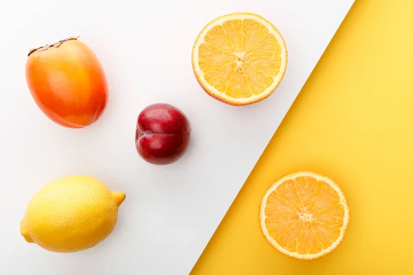 Vista superior de las mitades de naranja, caqui, limón y manzana sobre fondo amarillo y blanco - foto de stock