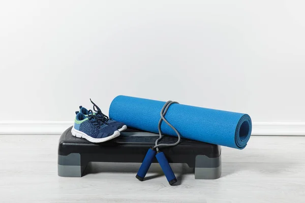 Plataforma de paso, colchoneta de fitness, cuerda de salto y zapatos deportivos en el suelo en casa - foto de stock