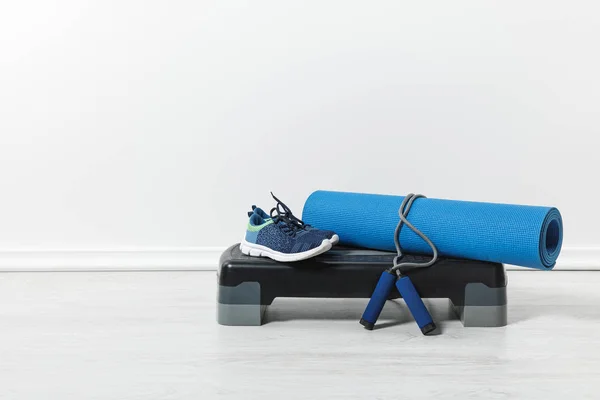 Plataforma del paso, estera azul de la aptitud, cuerda del salto y zapatos del deporte en el piso en casa - foto de stock