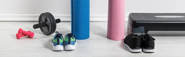 Панорамний знімок килимків для йоги, кросівок, крокової платформи та спортивного обладнання на підлозі вдома — стокове фото