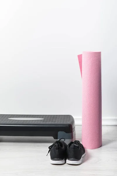 Plataforma paso, alfombra de fitness rosa y zapatillas de deporte en el suelo en casa — Stock Photo