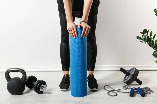 Vista cortada de esportista de pé com tapete de fitness em casa com equipamento desportivo — Fotografia de Stock