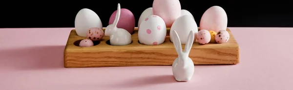 Conejitos blancos decorativos y huevos de Pascua sobre tabla de madera aislada sobre fondo negro, plano panorámico — Stock Photo
