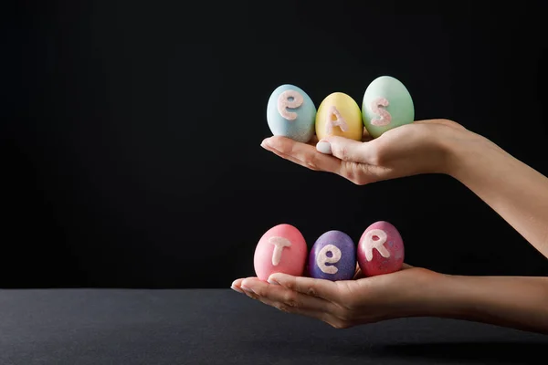 Vue recadrée de la femme tenant des œufs de poulet peints avec des lettres de Pâques sur noir et gris — Photo de stock