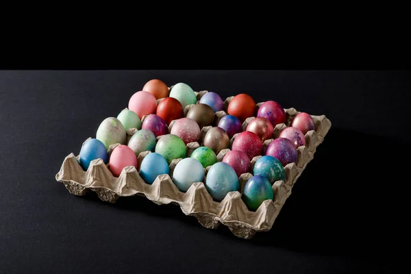 Plateau d'œufs avec des œufs de Pâques colorés sur fond gris et noir — Photo de stock