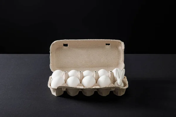 Egg tray with chicken eggs and decorative bunny on grey and black background — Stock Photo