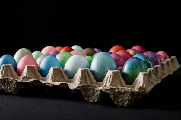 Enfoque selectivo de la bandeja de huevos con coloridos huevos de Pascua sobre fondo gris y negro - foto de stock