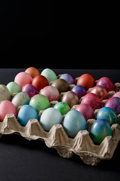 Plateau d'œufs avec des œufs de Pâques colorés sur fond noir — Photo de stock