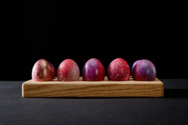 Ovos de Páscoa coloridos em tábua de madeira sobre fundo preto — Fotografia de Stock