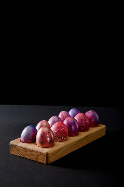 Цветные пасхальные яйца на деревянной доске на сером и черном фоне — стоковое фото