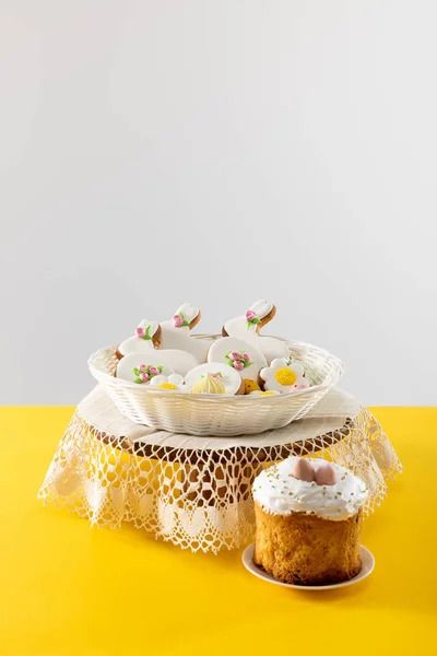 Вкусное печенье в плетеной корзине на круглой доске рядом с пасхальным тортом — стоковое фото