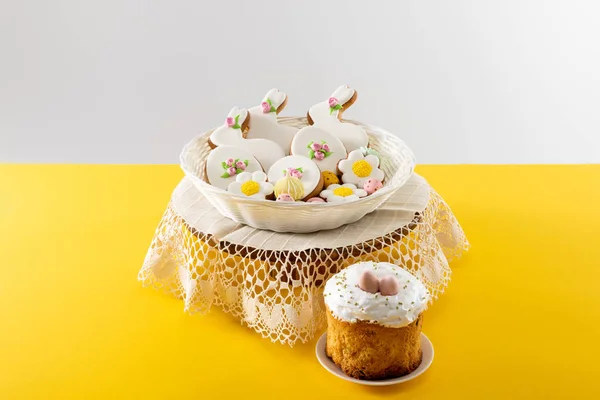 Deliciosos biscoitos em cesta de vime em tábua redonda perto de bolo de Páscoa isolado em fundo cinza — Fotografia de Stock