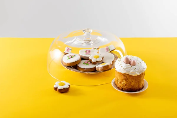 Bowl with tasty cookies covered by glass lid near easter cake isolated on grey background — Stock Photo