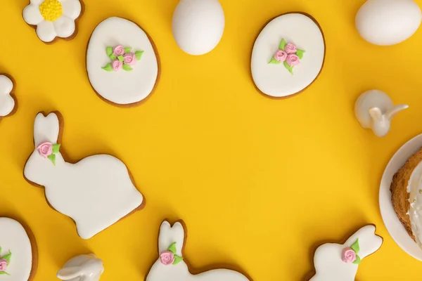Vista superior de ovos de galinha, biscoitos e coelhos decorativos no fundo amarelo — Fotografia de Stock