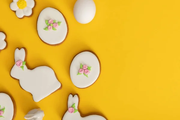 Vista dall'alto di uovo di pollo, biscotti e coniglietto decorativo su sfondo giallo — Foto stock