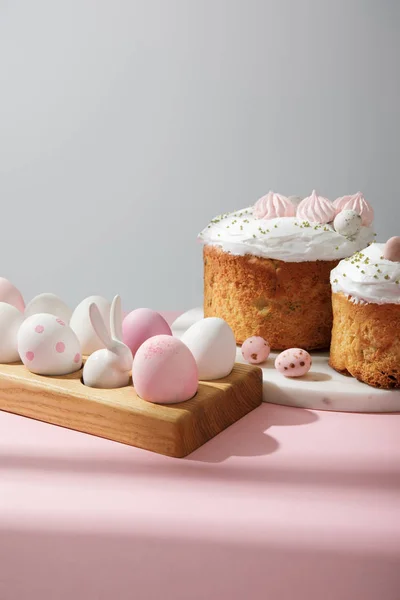 Ovos de Páscoa em tábua de madeira com coelho decorativo com bolos de Páscoa em rosa e cinza — Fotografia de Stock