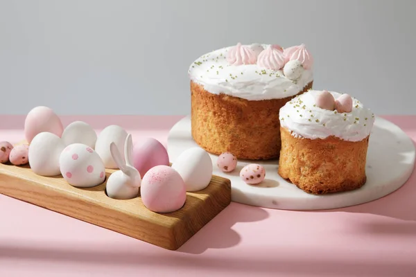 Easter eggs on wooden board with decorative bunny near easter cakes on pink and grey — Stock Photo