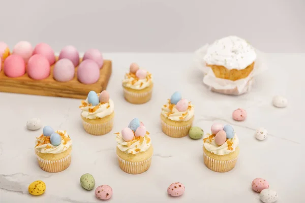 Cupcakes with painted chicken and quail eggs near traditional easter cake isolated on grey background — Stock Photo