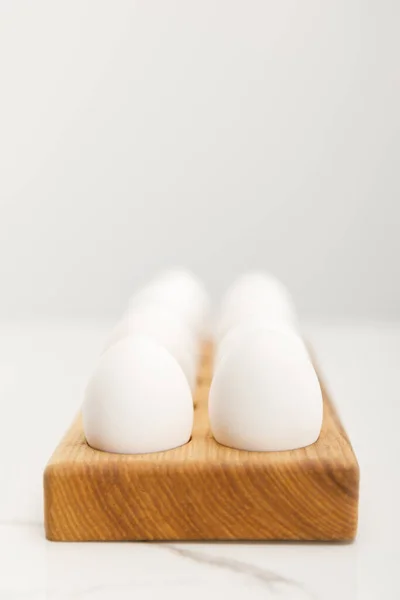 Enfoque selectivo de tablero de madera con huevos de pollo sobre fondo gris - foto de stock