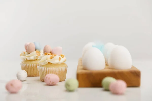 Enfoque selectivo de huevos coloridos de codorniz y pollo en tablero de madera con cupcakes de Pascua sobre fondo gris - foto de stock
