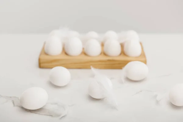 Concentration sélective des œufs de poulet sur le plateau à œufs en bois et des plumes sur le gris — Photo de stock