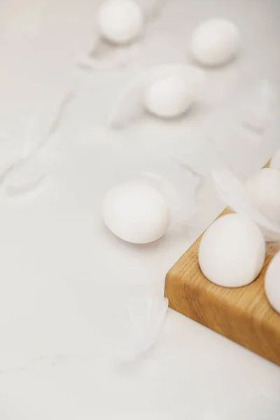 Selective focus of eggs on wooden egg tray and feathers on white background — Stock Photo