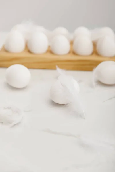 Enfoque selectivo de huevos sobre tabla de madera con plumas sobre fondo blanco - foto de stock