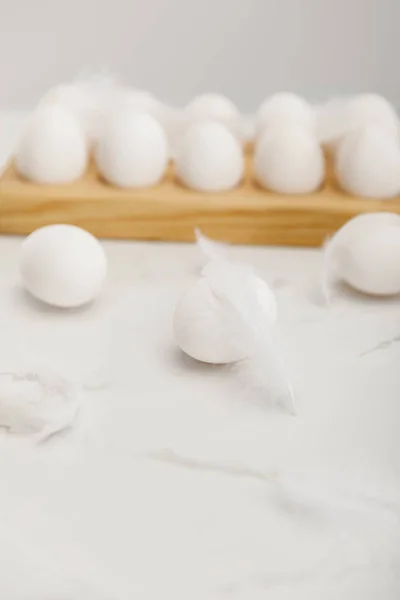 Selective focus of eggs on wooden board with feathers on white background — Stockfoto