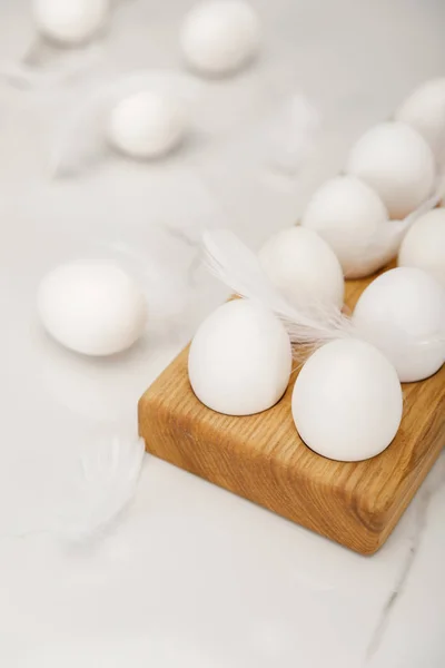 Selective focus of wooden egg tray with eggs and feathers on white background — Stockfoto