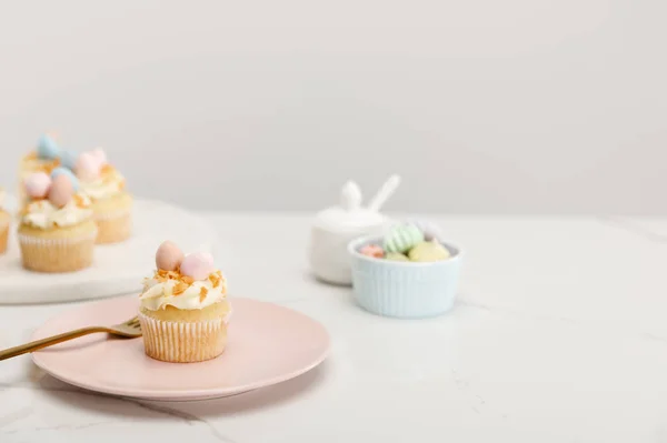 Focus selettivo di cupcake pasquali su piatto e tavola rotonda vicino zuccheriera su sfondo grigio — Foto stock