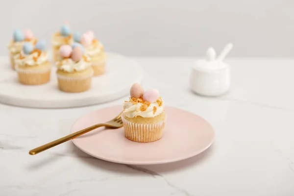 Enfoque selectivo de magdalenas en plato con tenedor y tabla redonda con azucarero sobre fondo gris - foto de stock