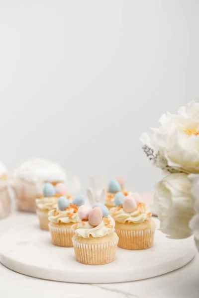 Foco seletivo de cupcakes em tábua redonda com flores em fundo cinza — Fotografia de Stock