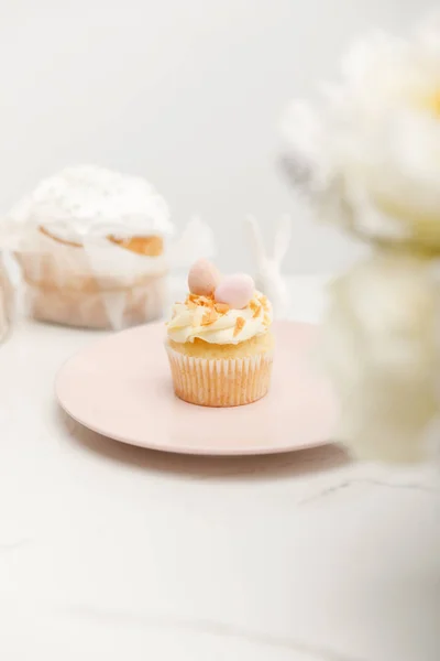 Foco seletivo de cupcake na placa e flores no fundo branco — Fotografia de Stock