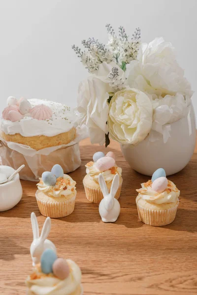 Enfoque selectivo de cupcakes con conejitos decorativos, azucarero, pan de Pascua y jarrón aislado en gris - foto de stock