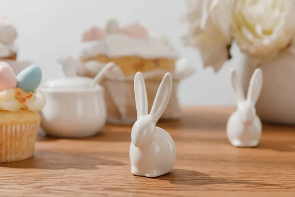 Foco seletivo de coelhos decorativos, cupcake, açucareiro e flores em fundo de madeira — Fotografia de Stock