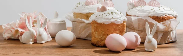 Conejitos decorativos, huevos de pollo, azucarero cerca de pasteles de Pascua y pétalos aislados en gris, plano panorámico - foto de stock